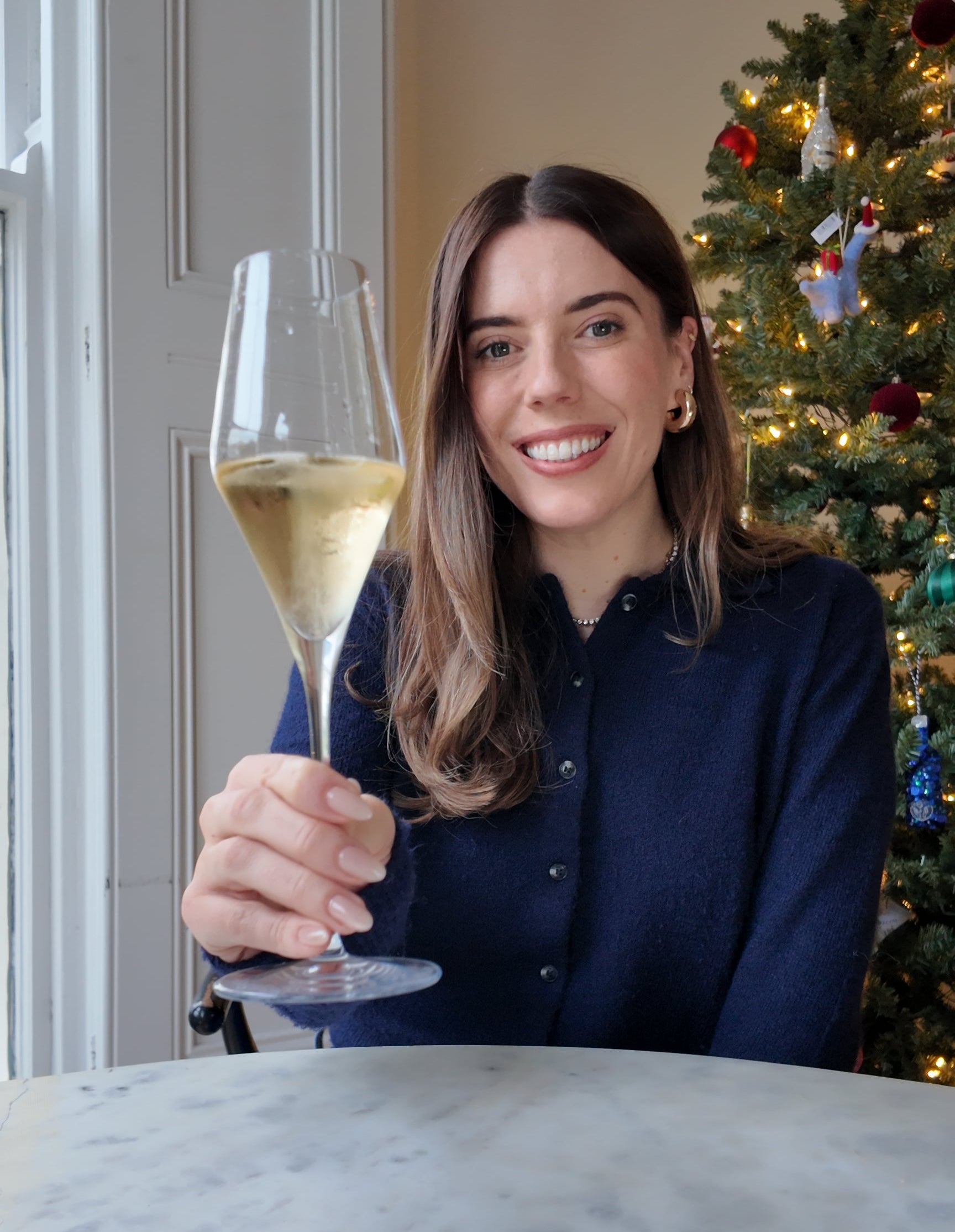 Woman holding a glass of champagne in front of a decorated Christmas tree.